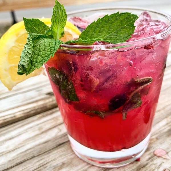 A vibrant red drink with ice, garnished with fresh mint and a lemon slice on a wooden table.