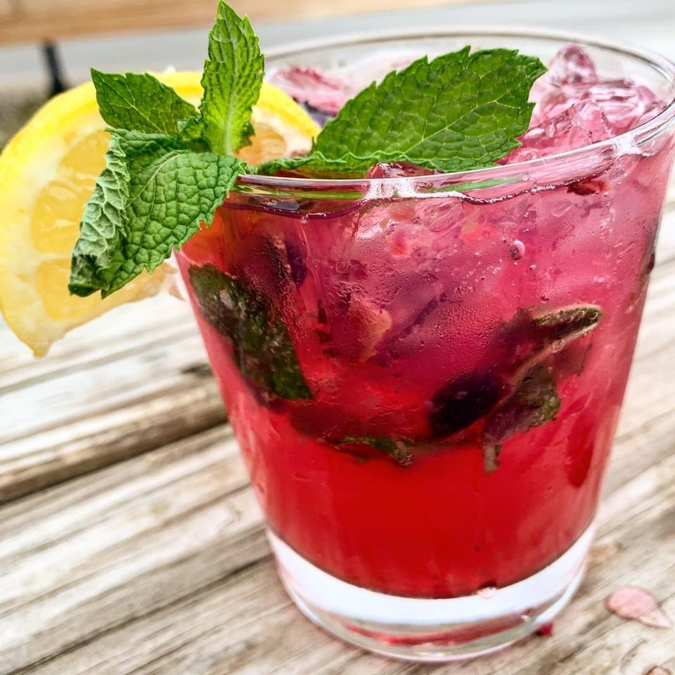 A vibrant red drink with ice, garnished with fresh mint and a lemon slice on a wooden table.