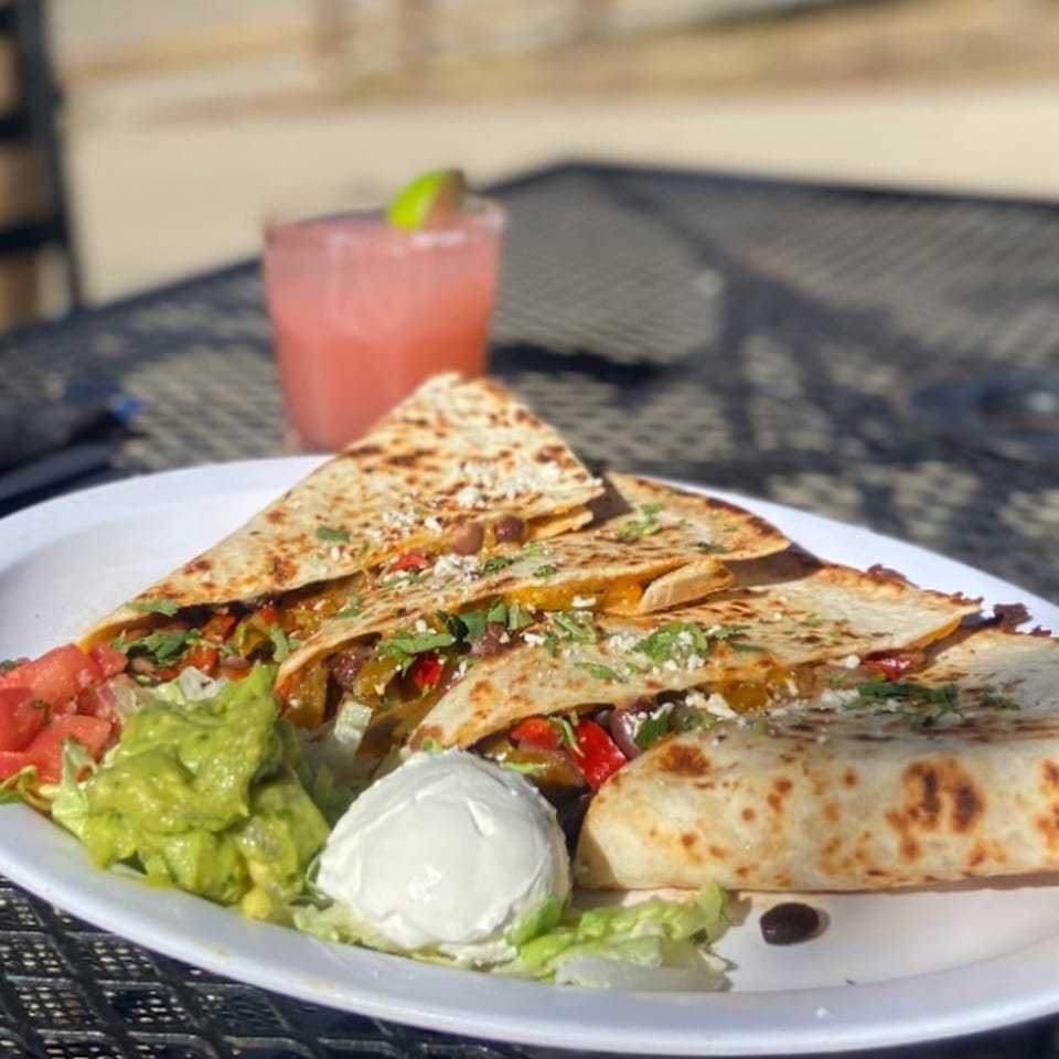 Yo Mommas Cantina quesadillas with guacamole, sour cream, and a pink margarita on a patio table.