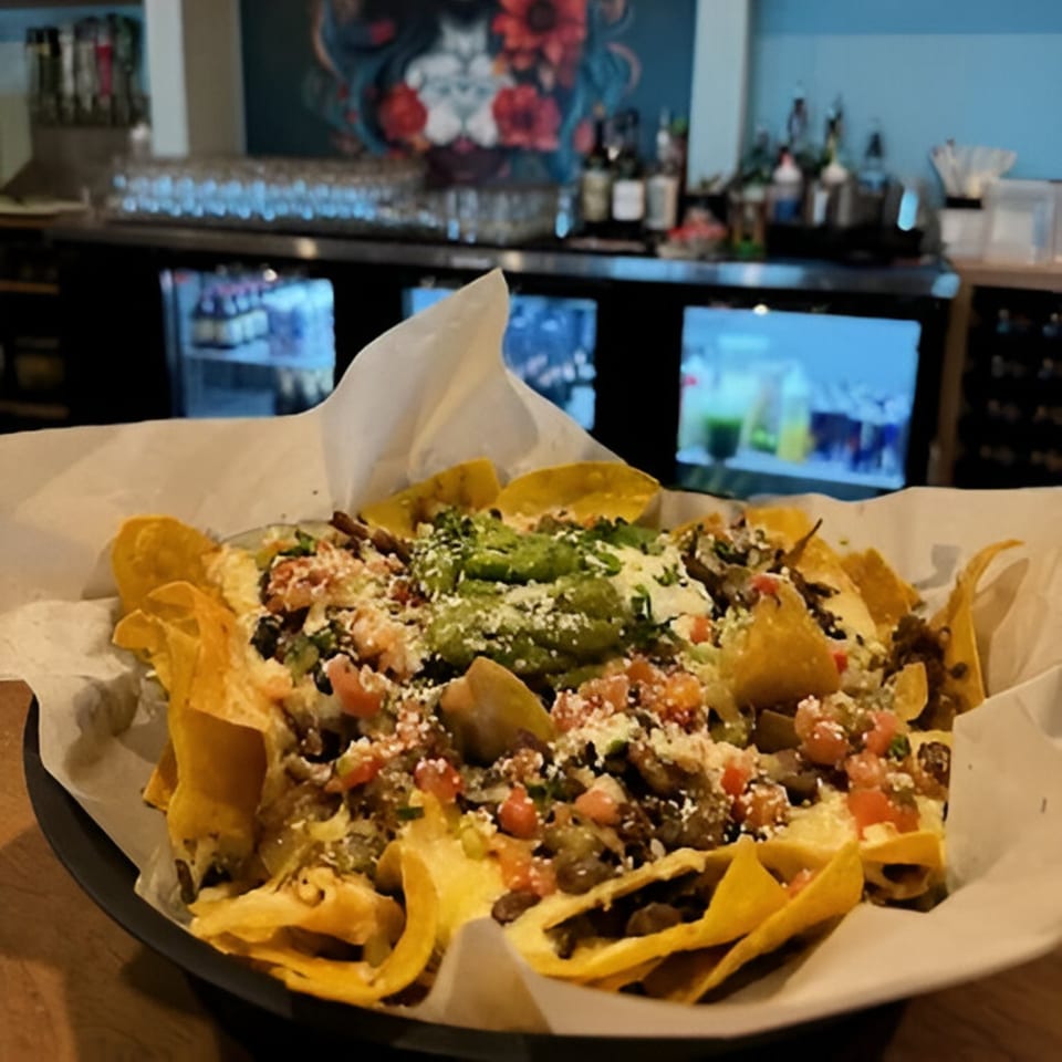 A large plate of Yo Mommas Cantina nachos with guacamole, cheese, and salsa, in a restaurant setting.