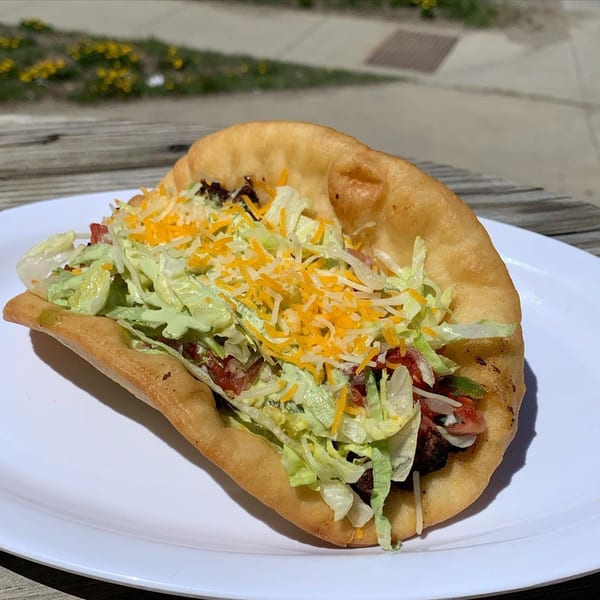 A golden-fried taco shell filled with seasoned meat, shredded lettuce, cheese, and creamy sauce.