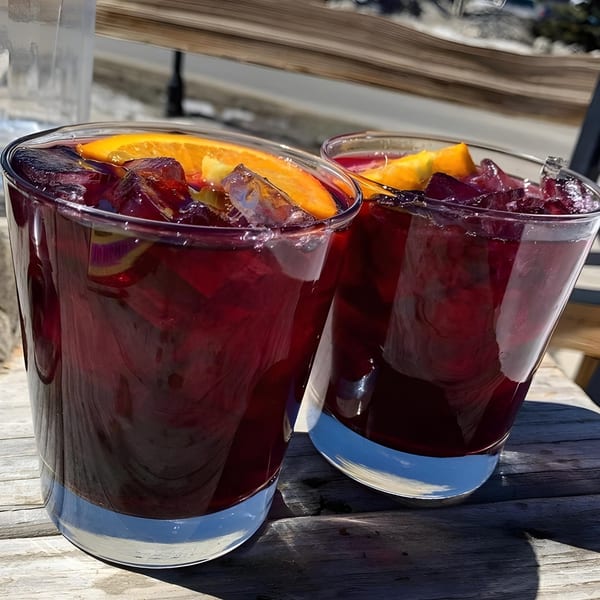 Two glasses of red sangria with orange slices and fruit on a wooden table.